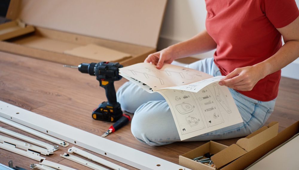 Woman,Sitting,On,Floor,Reading,Instruction,Manual,During,Furniture,Assembling. Woman,Sitting,On,Floor,Reading,Instruction,Manual,During,Furniture,Assembling.