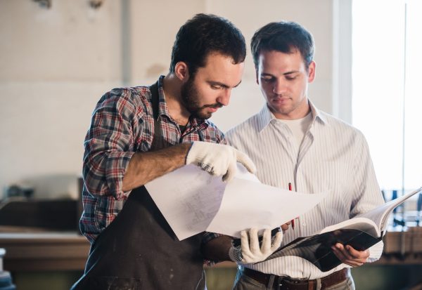 Happy,Male,Carpenter,Showing,Something,To,Coworker,At,His,Notebook