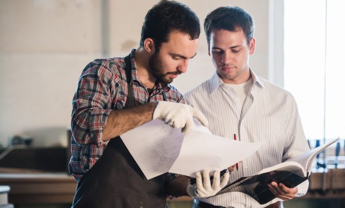 Happy,Male,Carpenter,Showing,Something,To,Coworker,At,His,Notebook