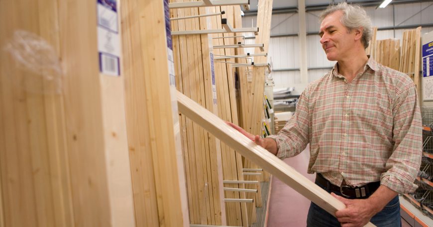 Woodworker selecting a board from a lumber yard rack for a beginner furniture project