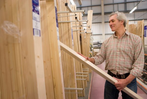 Mature,Man,Selecting,Timber,For,Diy,Project,In,Hardware,Store Woodworker selecting a board from a lumber yard rack for a beginner furniture project