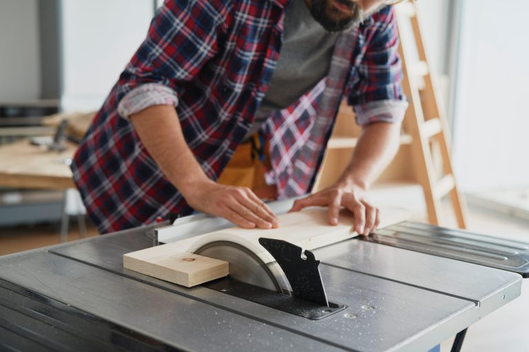 Woodworker cutting lumber with a table saw in a woodworking workshop