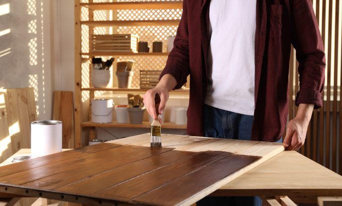Man,With,Brush,Applying,Wood,Stain,Onto,Wooden,Surface,Indoors, Applying polyurethane finish to a wooden surface with a brush for protection and durability