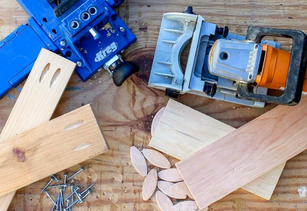 A top-down view of pocket hole jigs, a biscuit joiner, wood biscuits, and screws, illustrating common beginner woodworking joint types.