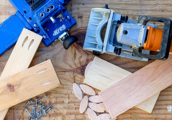A top-down view of pocket hole jigs, a biscuit joiner, wood biscuits, and screws, illustrating common beginner woodworking joint types.