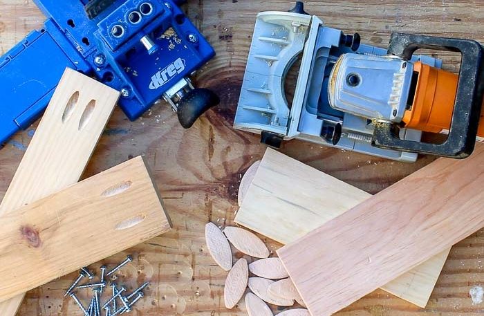 A top-down view of pocket hole jigs, a biscuit joiner, wood biscuits, and screws, illustrating common beginner woodworking joint types.