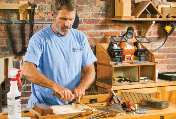 A woodworker using a sharpening stone at his workbench, demonstrating the setup for chisel and plane sharpening.