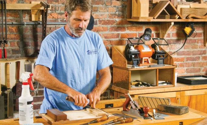 chisel-and-plane-sharpening-workshop.jpg A woodworker using a sharpening stone at his workbench, demonstrating the setup for chisel and plane sharpening.