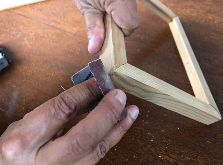 A person manually sanding a miter joint on a small wooden frame, showcasing simple wood joinery for beginners.